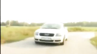 A blonde is having fun on the car hood with a guy in the street