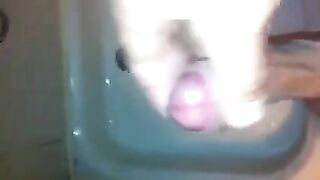 The kid caresses his dick under the shower head and plays with his cum
