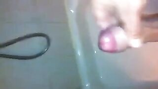 The kid caresses his dick under the shower head and plays with his cum