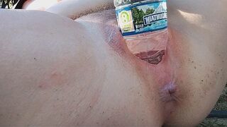 A busty MILF reaches intense pleasure while using a water bottle outdoors